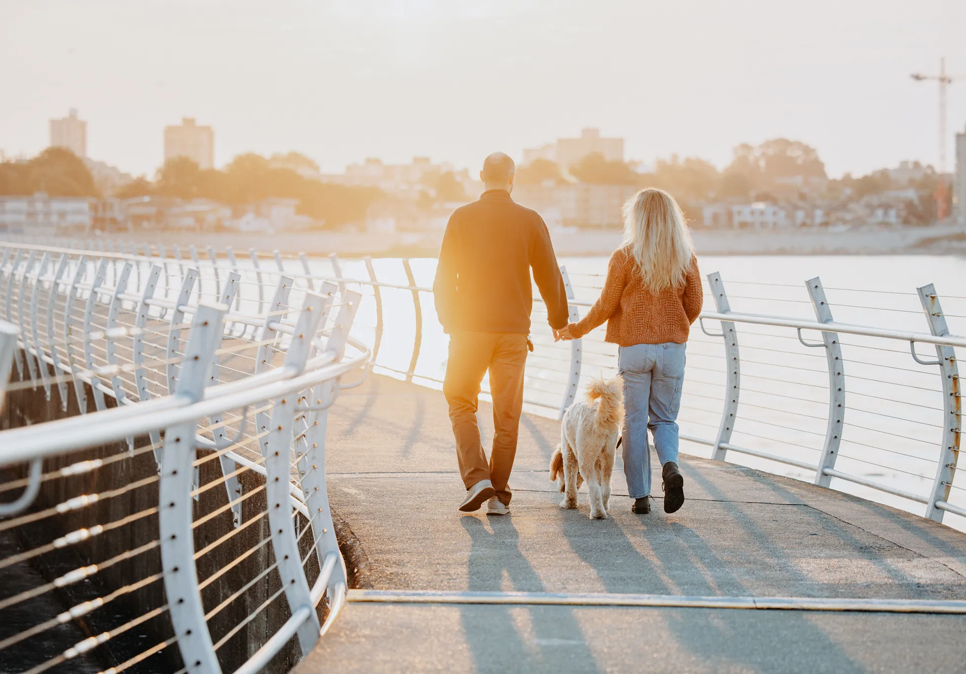Couple holding hands, walking dog on a bridge by the ocean